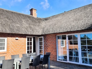 A brick building with a thatched roof, a patio with outdoor seating, and a glass door leading to an interior space. - 5 Star Holiday Home in Ulfborg (Ulfborg)