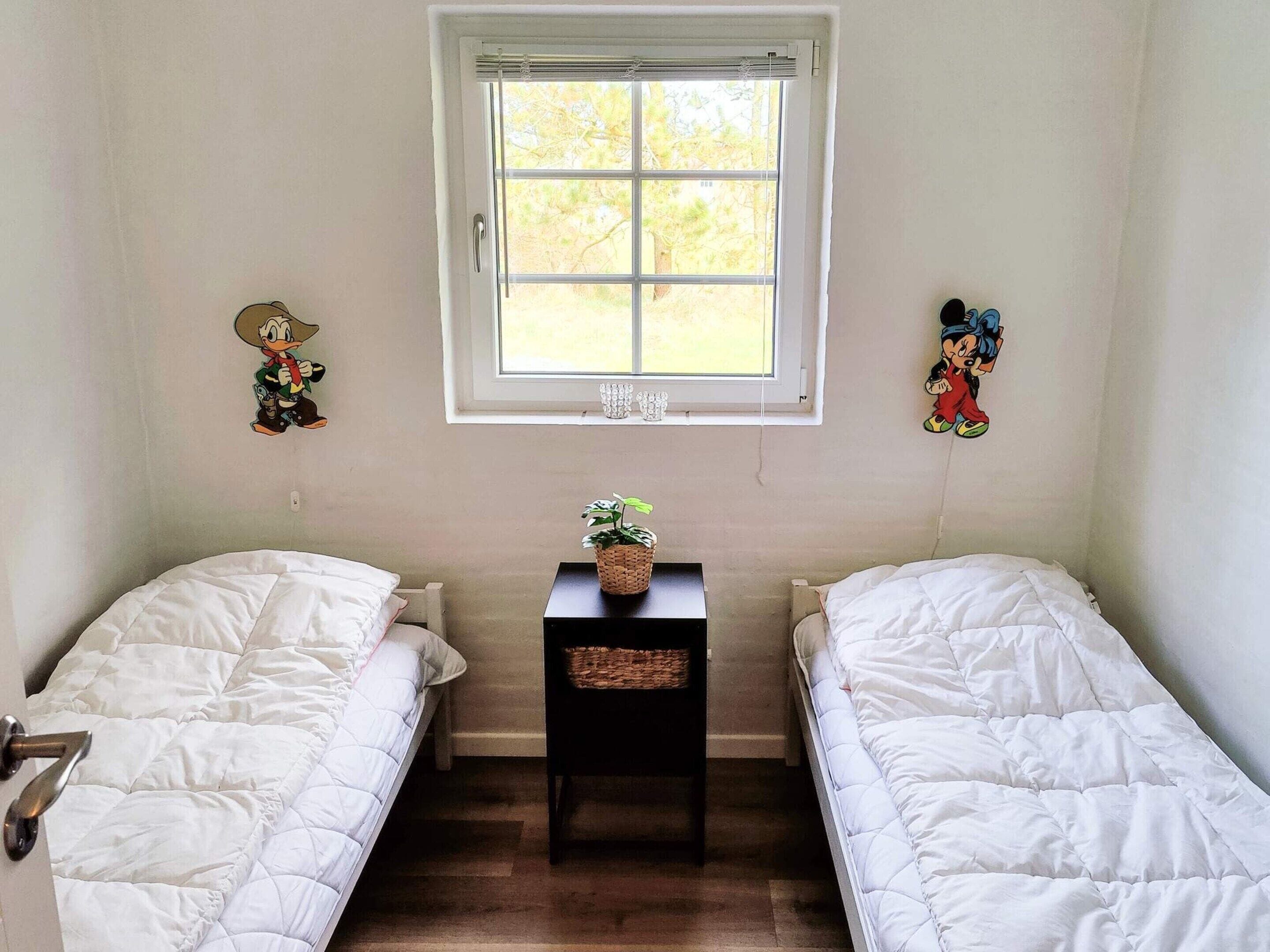 Ein Zimmer mit zwei Einzelbetten, einem kleinen Tisch mit Pflanze und einem Fenster mit Jalousien.