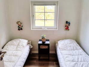 A room with two single beds, a small table with a plant, and a window with blinds.