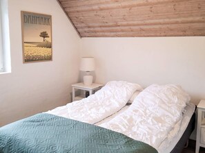 Quarto com cama, mesa de cabeceira, abajur e um pôster na parede.