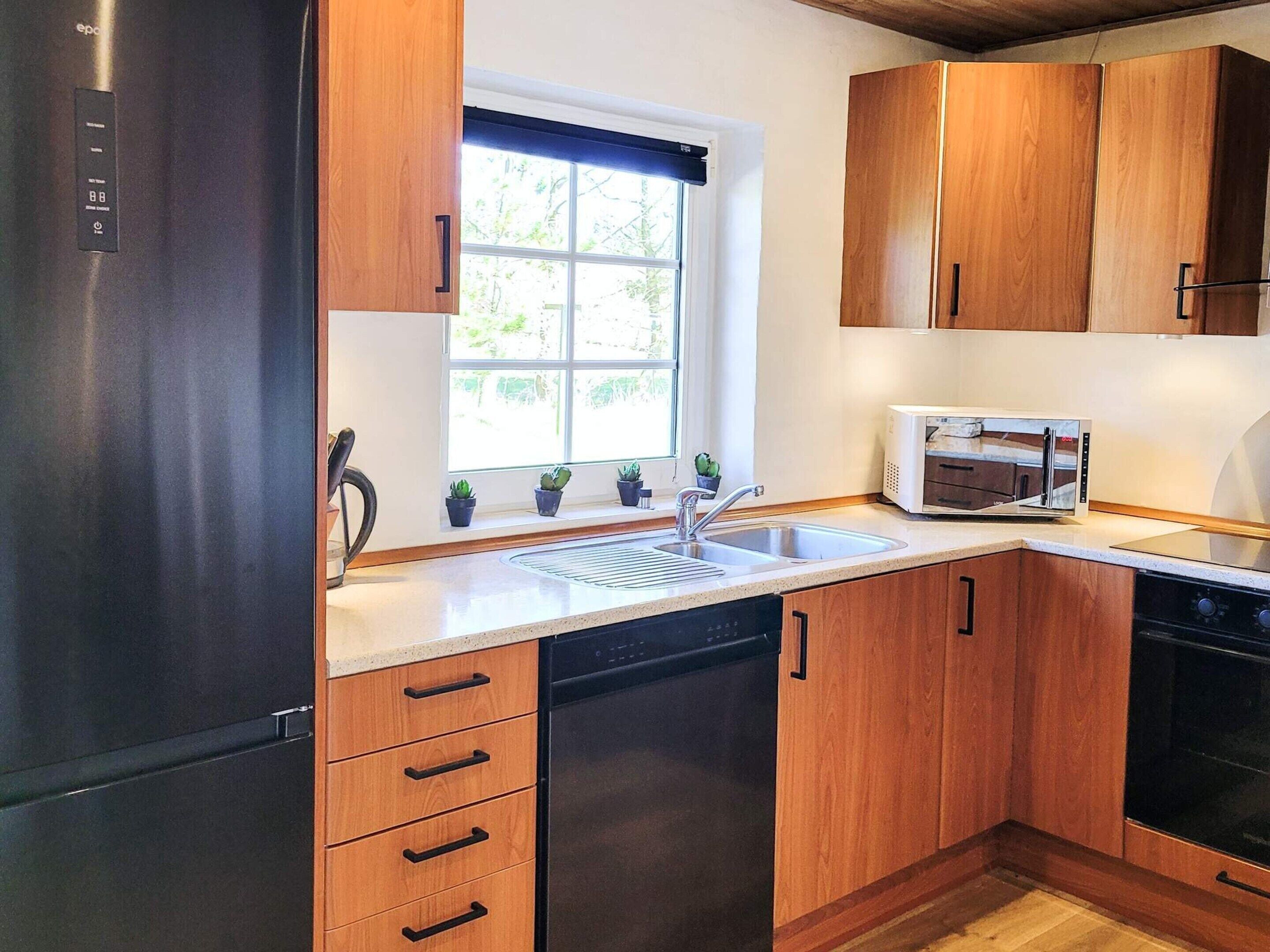 A kitchen with wooden cabinets, a stainless steel refrigerator, a microwave, and a dishwasher.