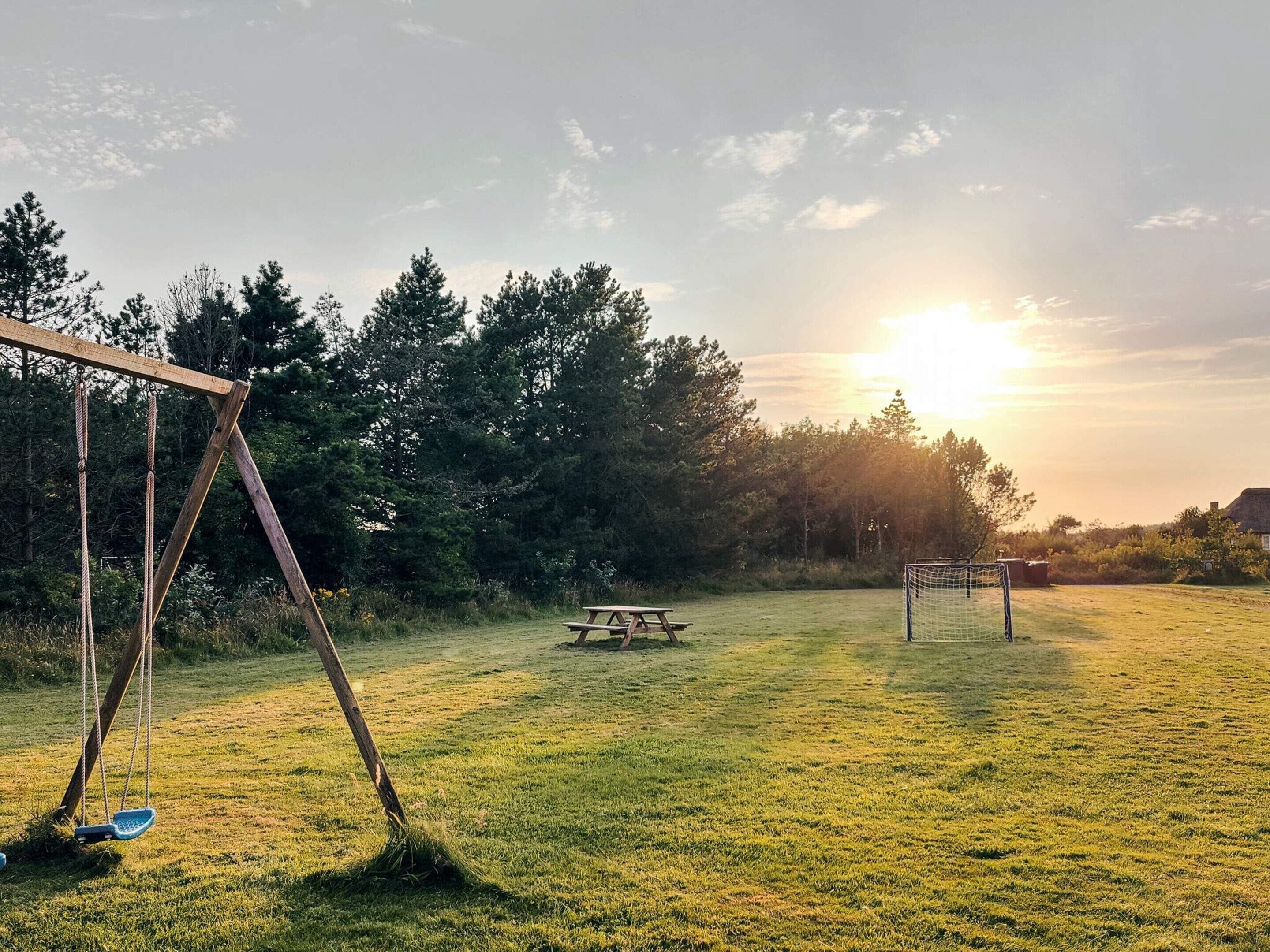 A grassy field with a swing set, picnic table, and soccer goal.