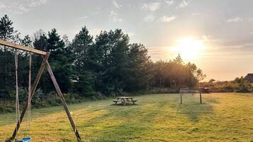 A grassy field with a swing set, picnic table, and soccer goal.
