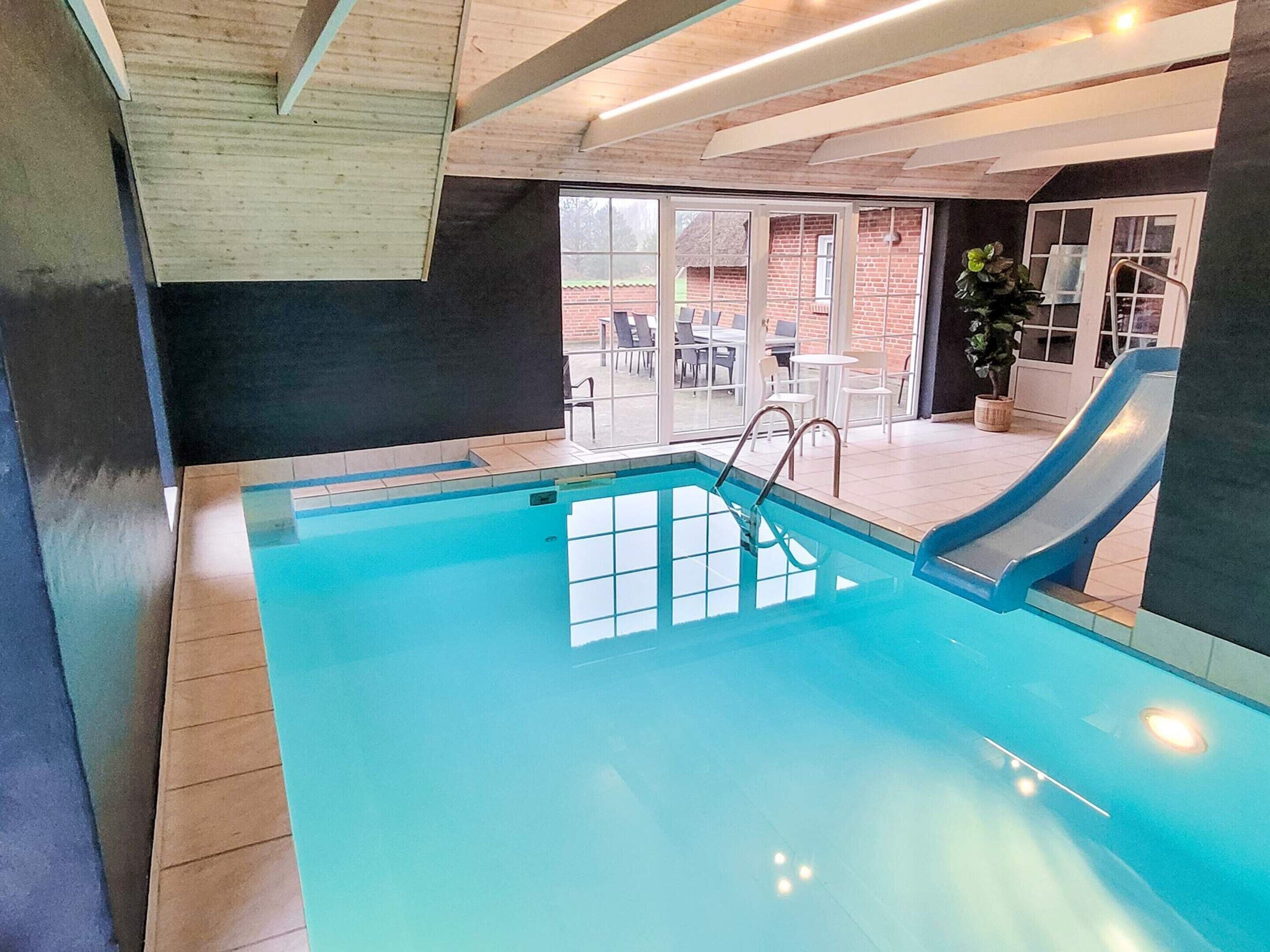 An indoor swimming pool with a slide, wooden ceiling, and a view of the outside patio area.