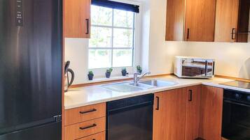 A kitchen with wooden cabinets, a stainless steel refrigerator, a microwave, and a dishwasher.