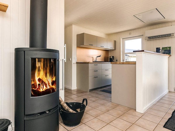 A modern kitchen with a wood-burning stove, white cabinetry, and a small island with a sink.