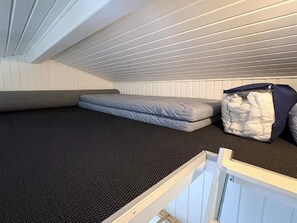 Un pequeño dormitorio en el ático con un colchón, un baúl y una ventana.
