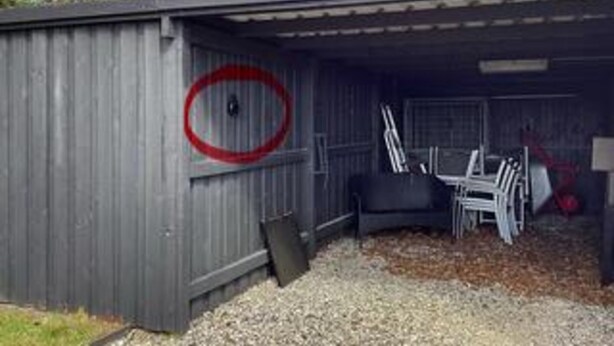 Ett metallskjul med en röd cirkel som markering, ett underlag av grus och några stolar inuti.