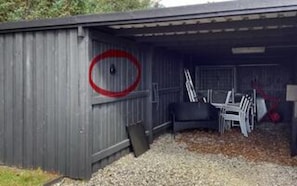 A metal shed with a red circle marking, gravel ground, and a few chairs inside.