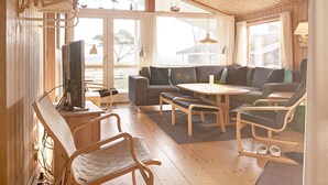 A cozy room with a wooden ceiling, a sofa, a small table, and a TV. - Seaside Escape in Snogebaek - By Traum Ferienwohnungen (Nexø)