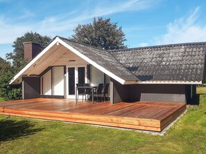 A modern house with a sloped roof, a wooden deck, and a glass door leading to an outdoor seating area.