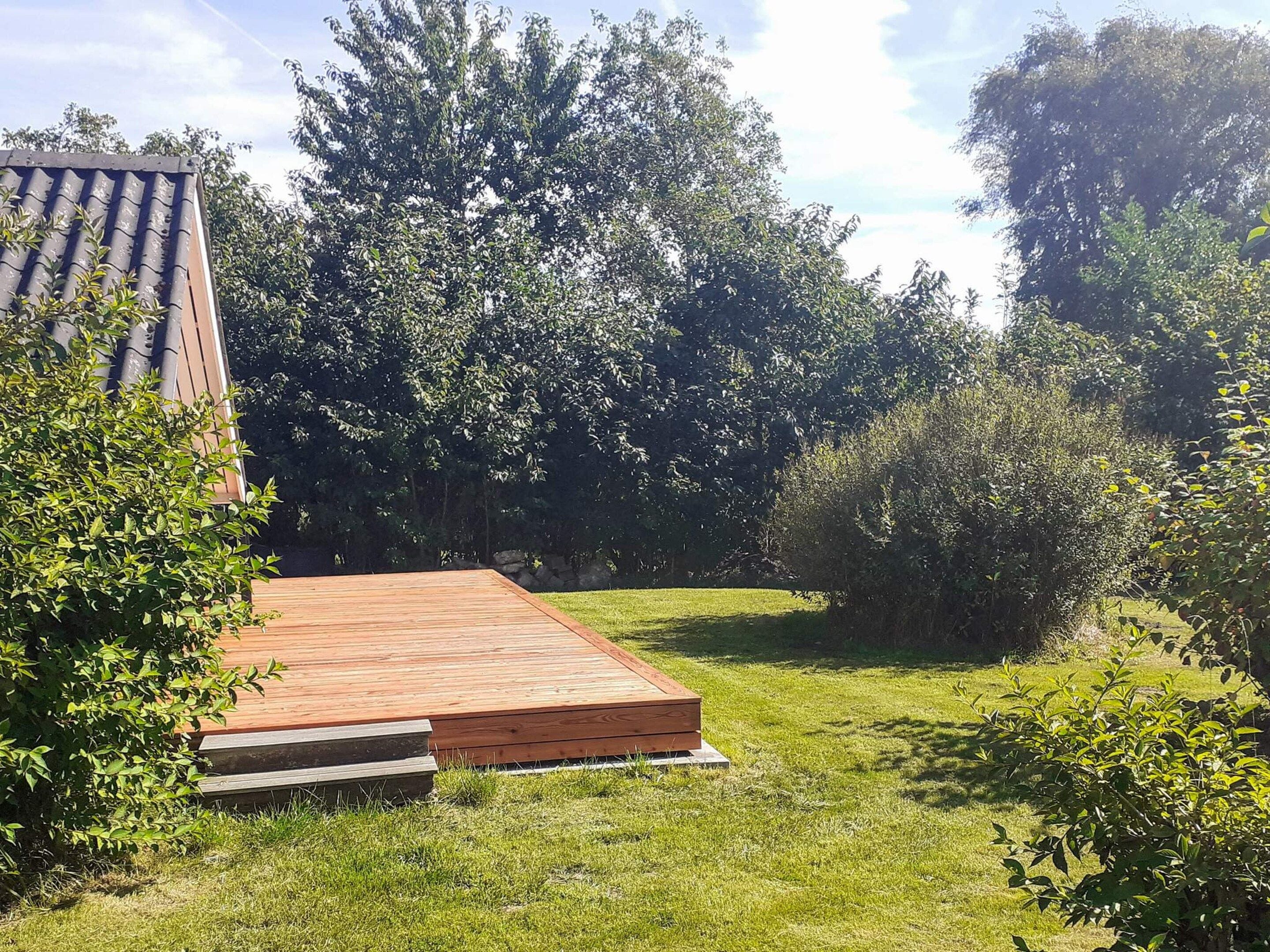 Una terraza de madera con un área verde y árboles al fondo.