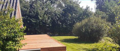 Una terraza de madera con un área verde y árboles al fondo.