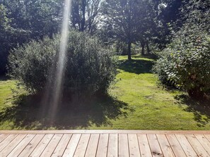 A wooden deck with a grassy lawn and dense shrubbery.