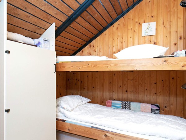 A bunk bed with a wooden ceiling and a white wardrobe.
