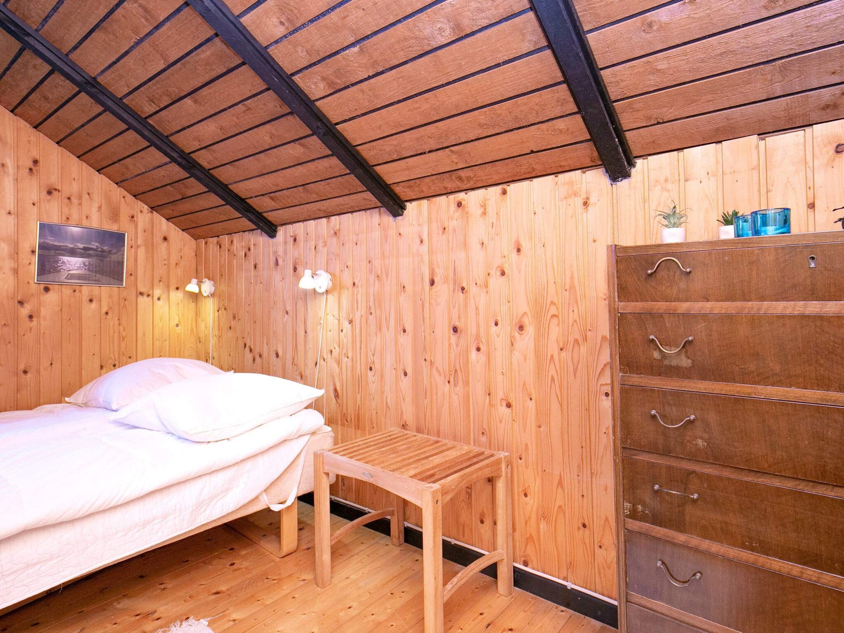 Quarto de madeira com cama, um banco e uma cômoda.