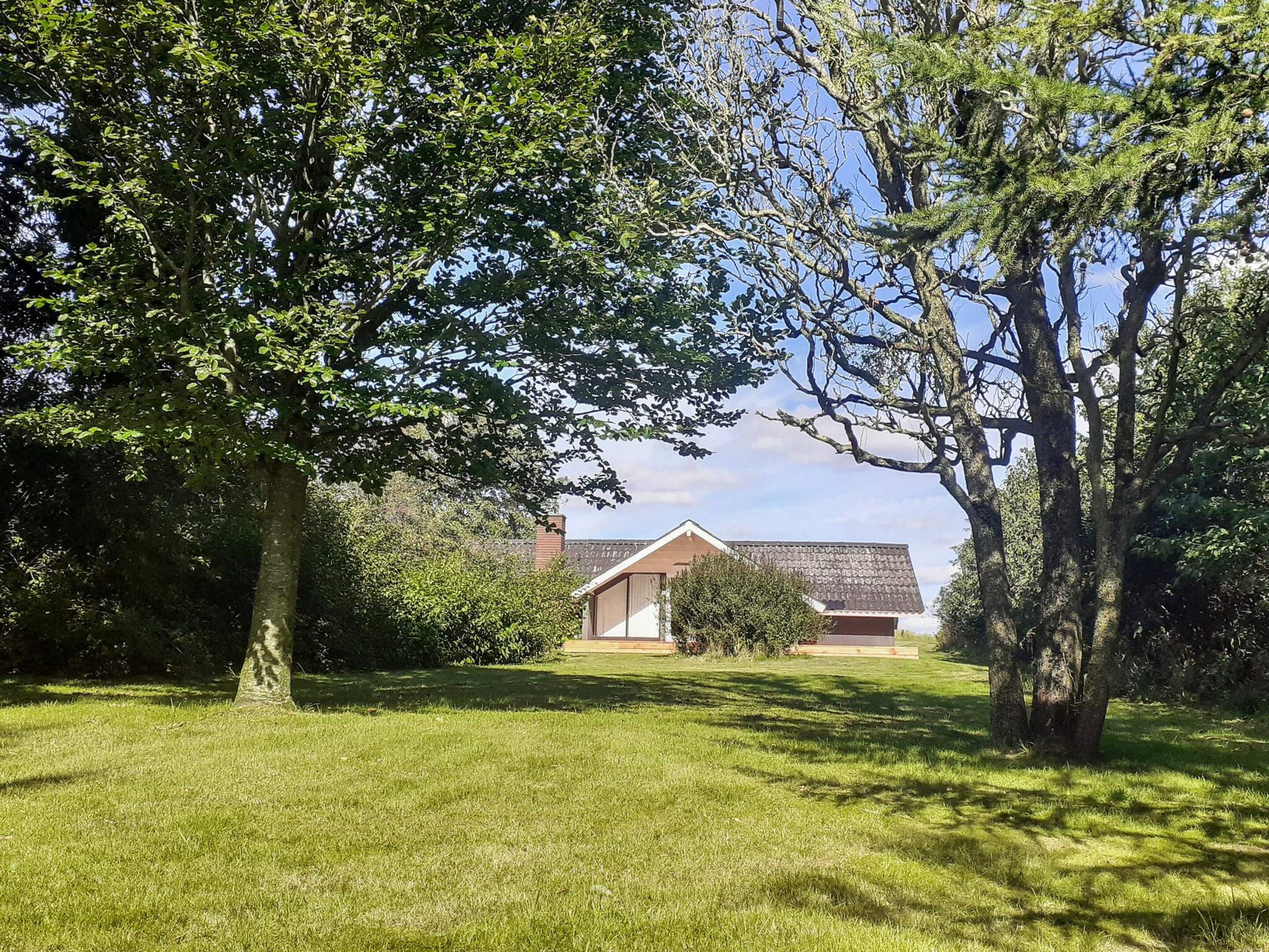 Une zone herbeuse avec des arbres et, au fond, un bâtiment doté d’un toit rouge.