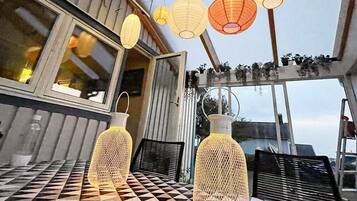 A dining area with a checkered table, two hanging paper lanterns, and a view through a window.