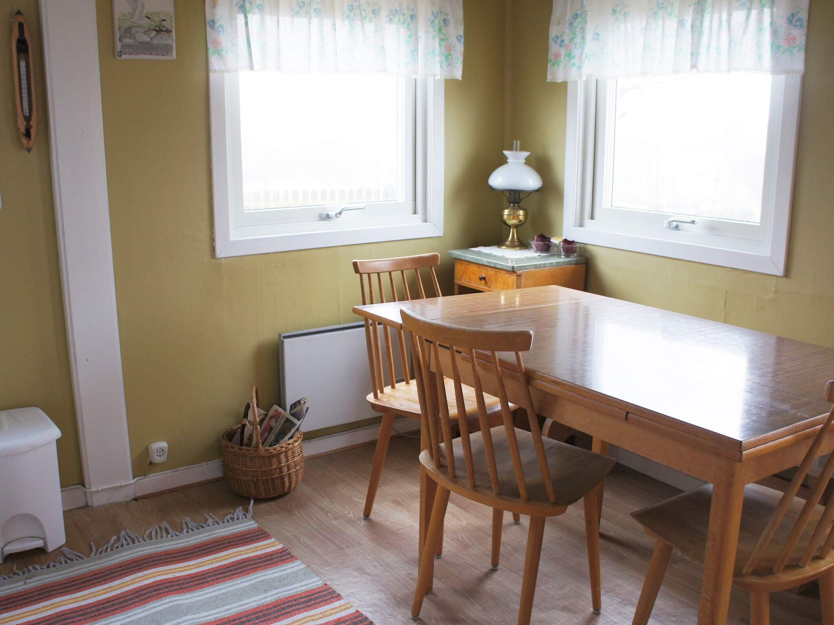 A dining area with a wooden table and chairs, a radiator, a lamp, and a window with curtains.