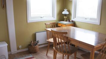 A dining area with a wooden table and chairs, a radiator, a lamp, and a window with curtains.