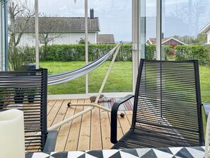 Eine Terrasse mit zwei schwarzen Netzstühlen, einer Hängematte und Blick auf ein Haus und einen Garten.