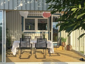 An outdoor dining area with a table and chairs, surrounded by a wooden deck and a window with curtains. - 8 Person Holiday Home in Tvaaker (Tvaaker)