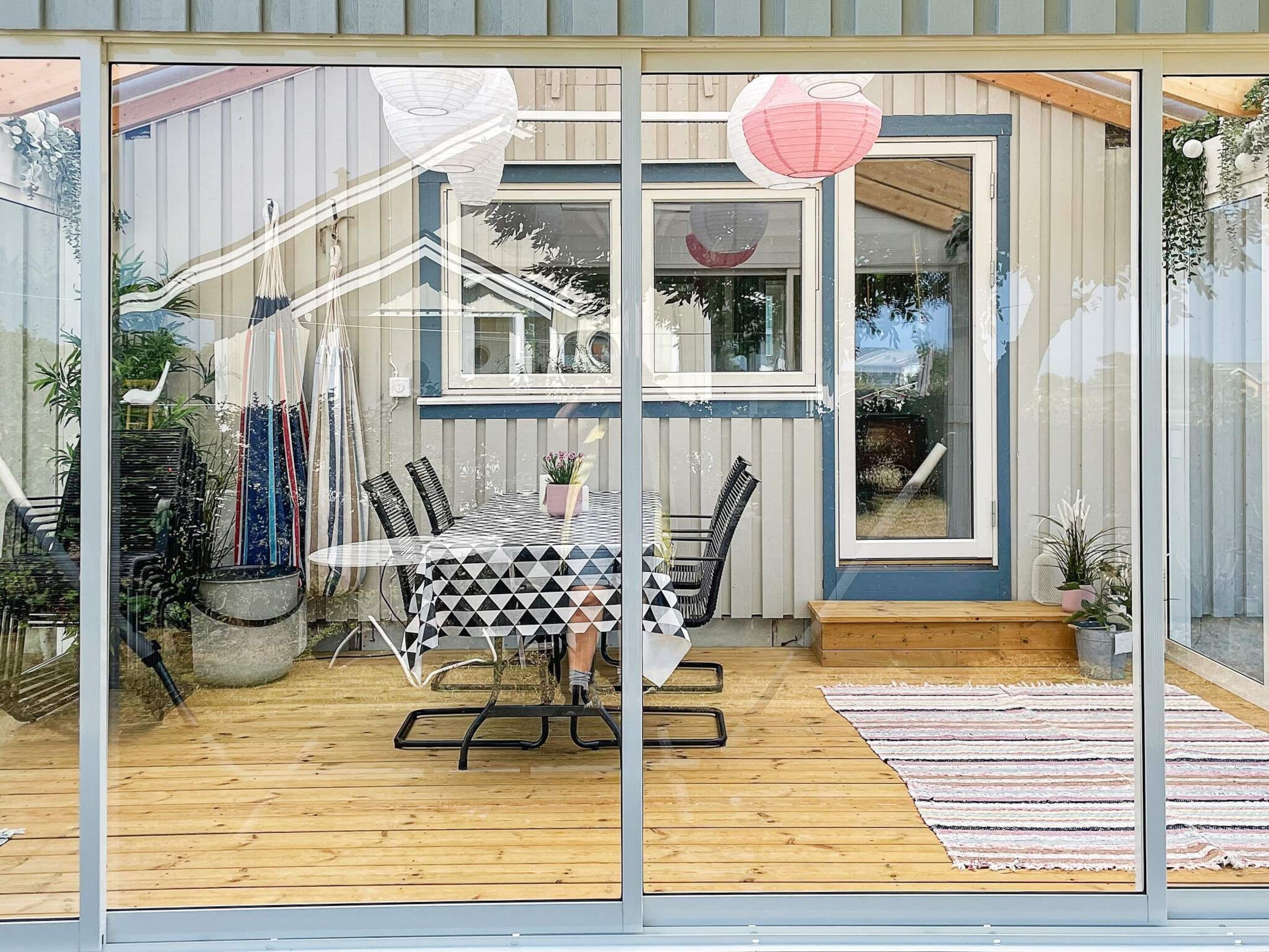 A glass-enclosed patio with a wooden deck, a table with chairs, and potted plants.