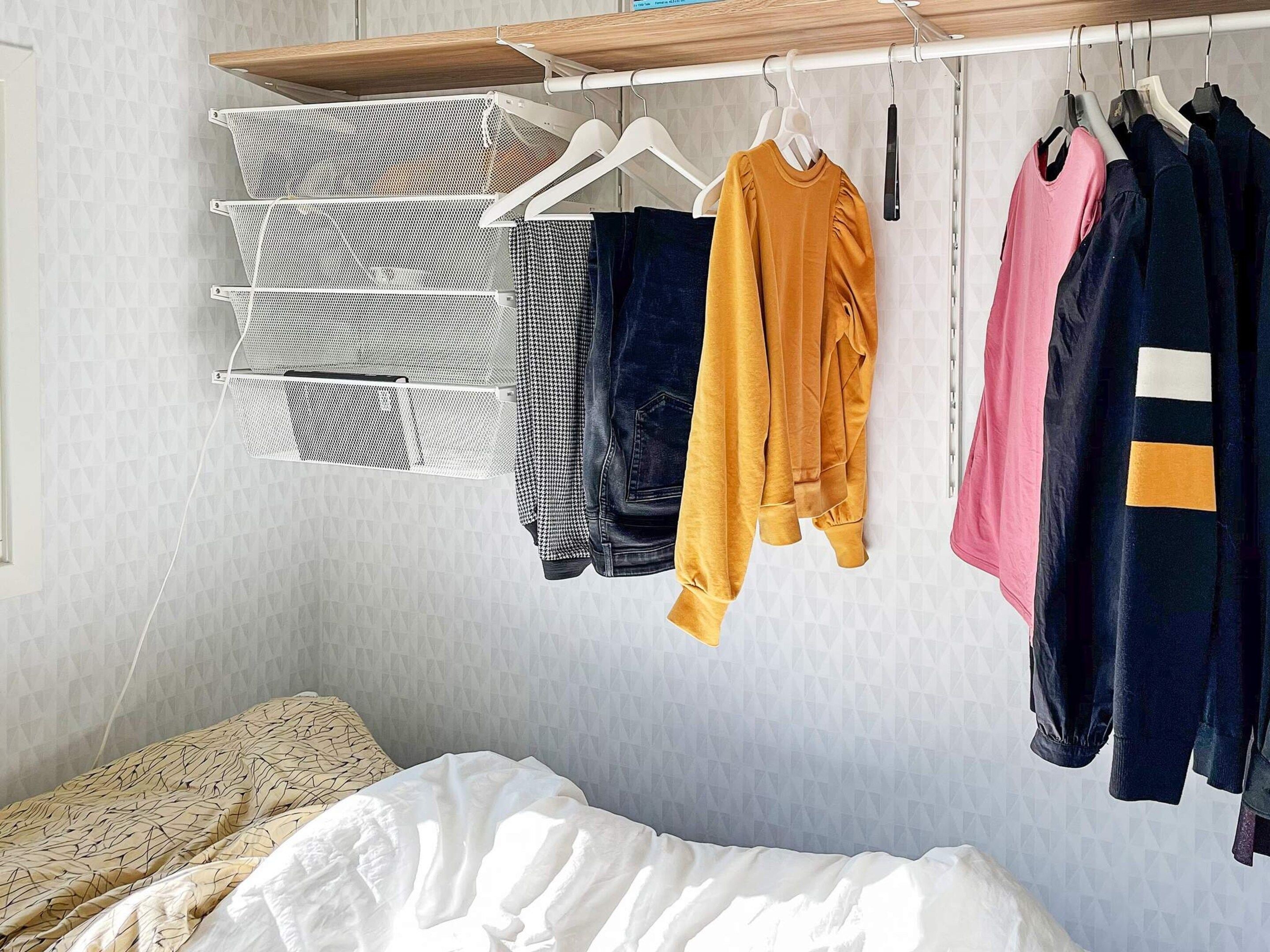 Un dormitorio con una cama, un perchero con ropa y una estantería en la pared.