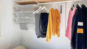 Un dormitorio con una cama, un perchero con ropa y una estantería en la pared.