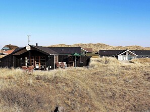 A rustic cabin with a porch and outdoor seating, surrounded by dry grass and hills. - 4 Star Holiday Home in Hvide Sande (Hvide Sande)