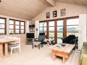 A cozy room with a wooden floor, a dining table, a TV, and a large window offering a view of the beach. - 4 Star Holiday Home in Hvide Sande (Hvide Sande)