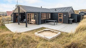 A black wooden building with a sloped roof, a deck, and a sand-filled depression. - 4 Star Holiday Home in Hvide Sande (Hvide Sande)