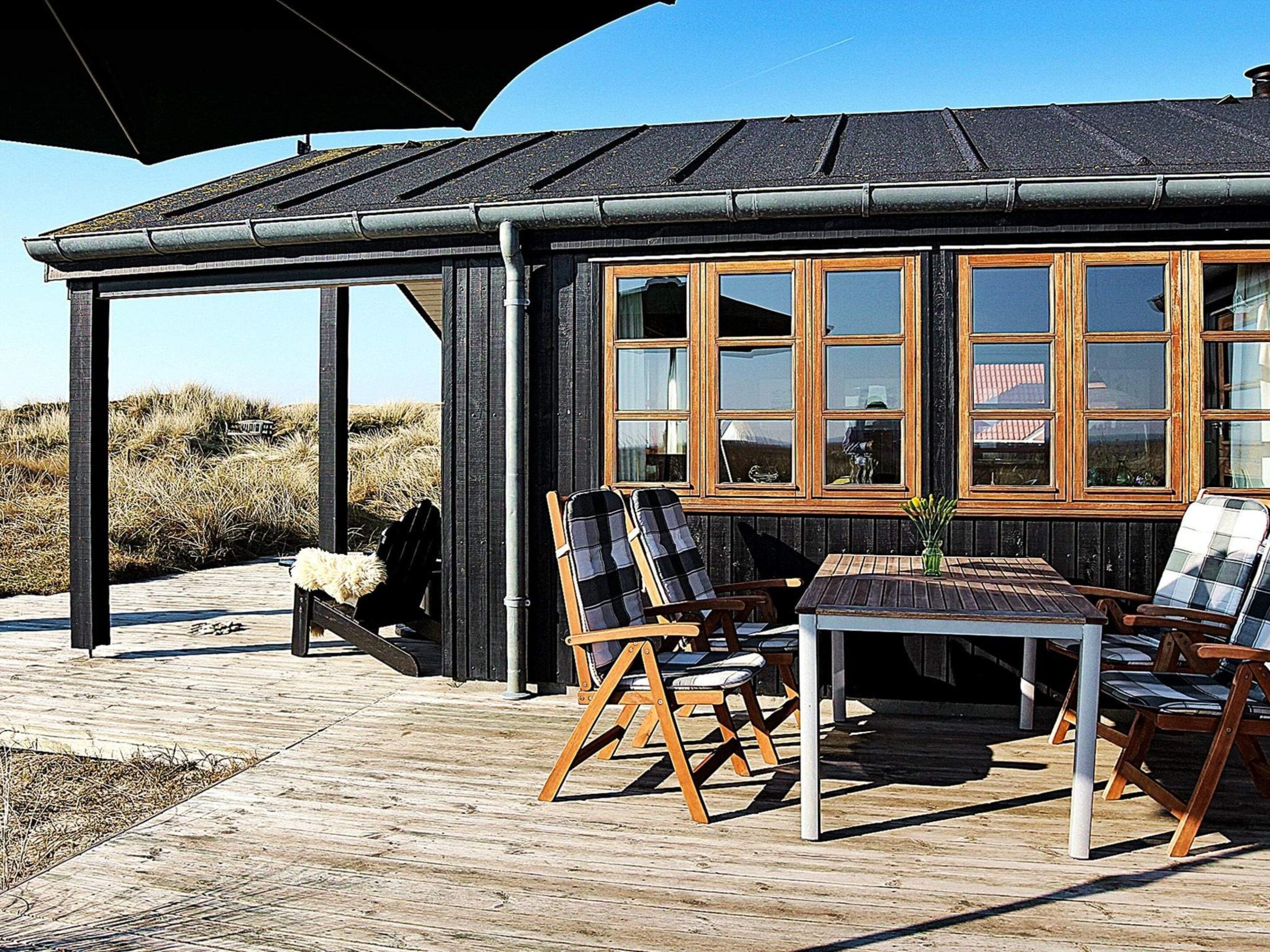 Une structure en bois dotée de grandes fenêtres, avec une table et des chaises à l’extérieur.