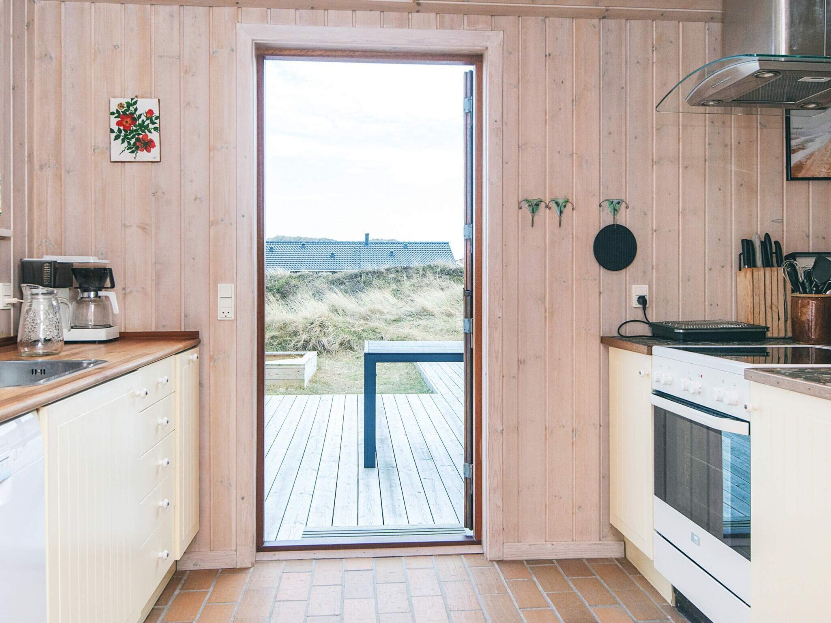 A modern kitchen with wooden paneling, a large window, and a view of the beach.