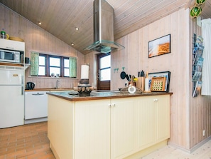 A kitchen with a central island, wooden panel walls, a stainless steel range hood, and a window with curtains. - 4 Star Holiday Home in Hvide Sande (Hvide Sande)