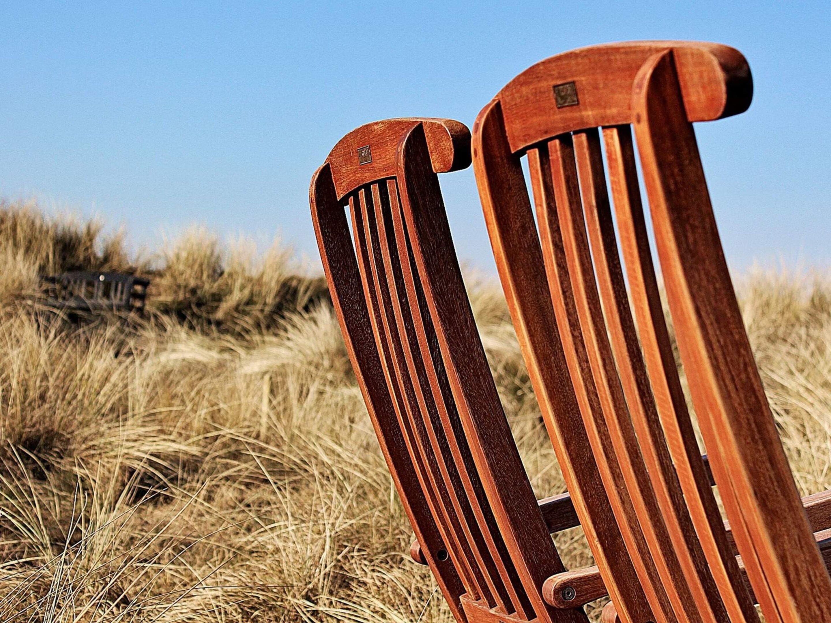 Two wooden chairs with vertical slats, positioned in a natural setting with dry grass.