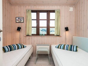 A small, cozy room with two single beds, a window with checkered curtains, a radiator, and a small table.