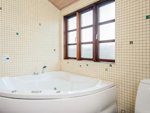 Un baño con una bañera grande, paredes enlosetadas, una ventana y un inodoro.