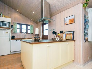 A kitchen with wooden paneling, a central island, a microwave, a kettle, and a hanging pot rack.