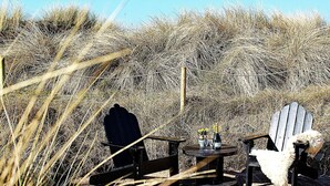 A wooden deck with two Adirondack chairs and a small round table with a bottle and flowers. - 4 Star Holiday Home in Hvide Sande (Hvide Sande)