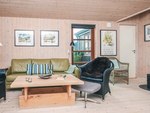 A cozy living room with a green sofa, a wooden coffee table, and a wicker chair. There are framed pictures on the walls and a door with a window. - 4 Star Holiday Home in Hvide Sande (Hvide Sande)