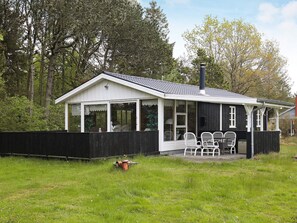 A small, single-story building with a white exterior and a black roof, surrounded by a wooden fence and a grassy area. - 4 Person Holiday Home in Hals (Hals)