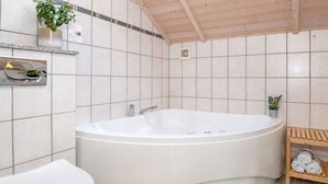 A modern bathroom with a freestanding bathtub, a toilet, and a shelf with towels. - 5 Star Holiday Home in Ulfborg (Ulfborg)