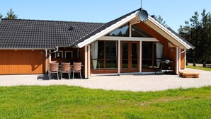 A modern house with a sloped roof, large windows, and a patio area with outdoor furniture. - 5 Star Holiday Home in Ulfborg (Ulfborg)