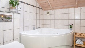 A bathroom with a freestanding bathtub, a toilet, a shelf with toiletries, and a small potted plant. - 5 Star Holiday Home in Ulfborg (Ulfborg)