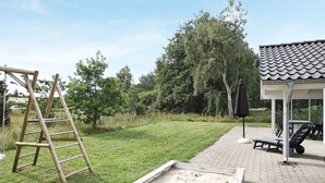 A backyard with a wooden ladder, a sandbox, and outdoor furniture including a table and chairs.