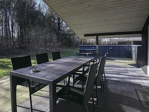 Una terrazza esterna con tavolo e sedie, una zona coperta e un cortile recintato.