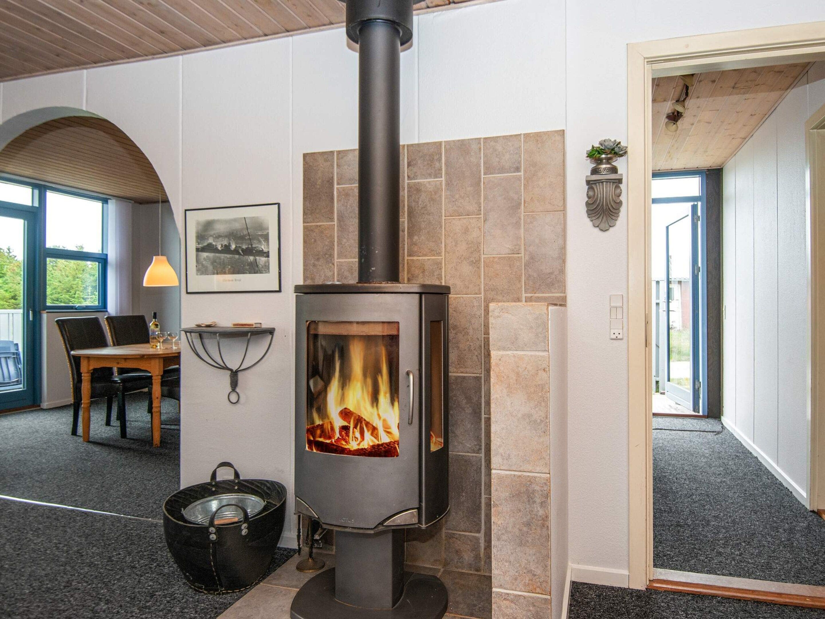 A modern interior with a wood-burning stove, a dining area with a table and chairs, and a view through an arched doorway.