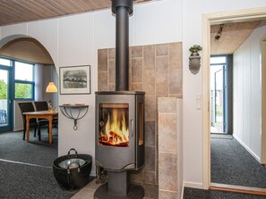 A modern interior with a wood-burning stove, a dining area with a table and chairs, and a view through an arched doorway.