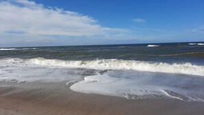 A beach with waves approaching the shore, clear sky, and distant horizon. - 6 Person Holiday Home in Hvide Sande (Hvide Sande)